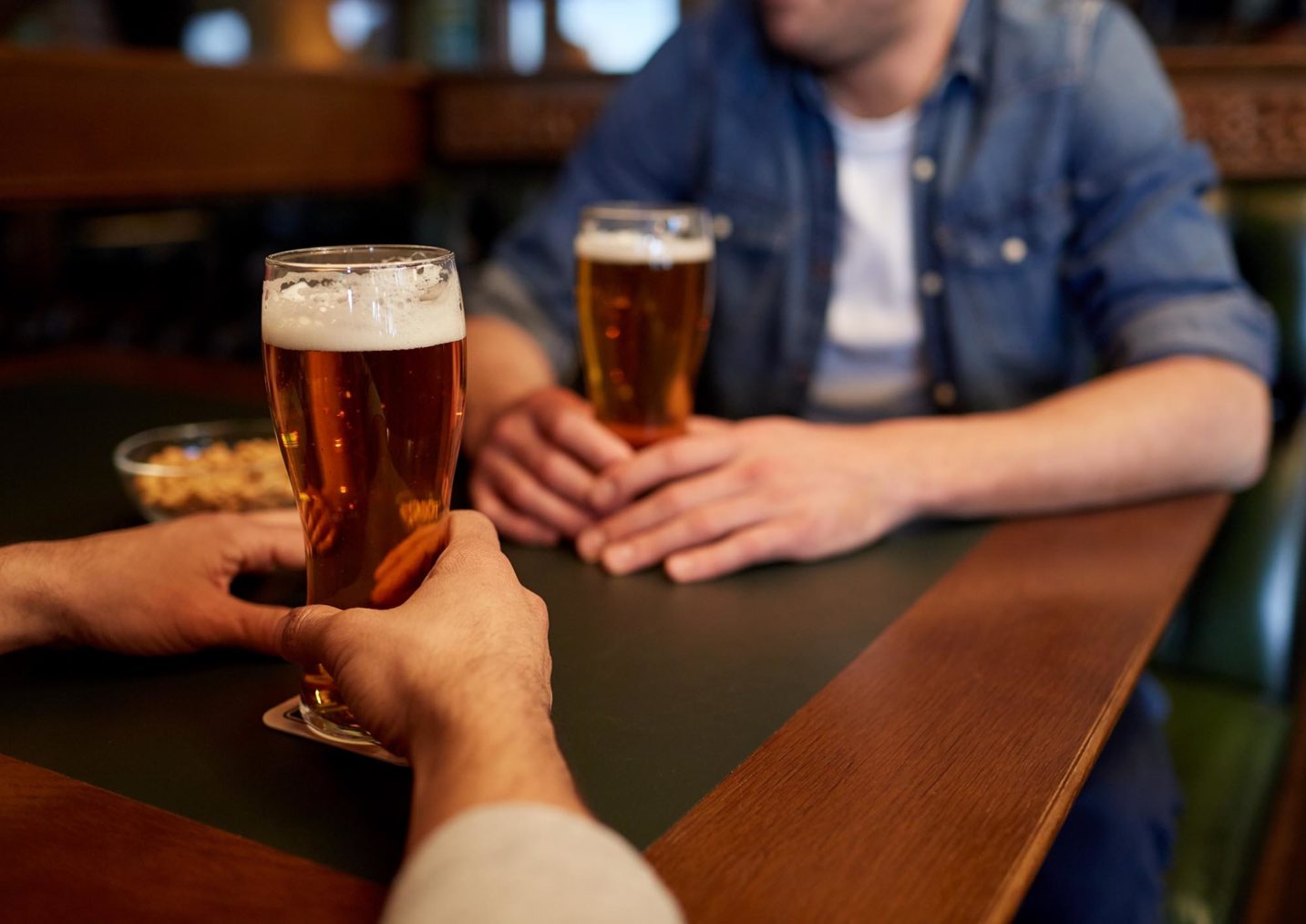 Nærbilde av to ølglass på et bord. Hendene til to personer holder rundt hvert sitt glass.