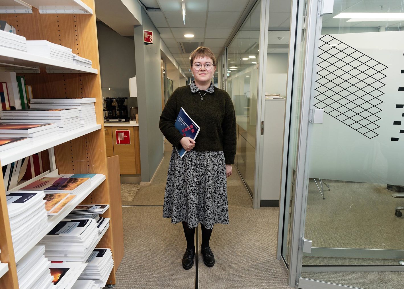 Mina Haugen står i en korridor med rapporten under armen.