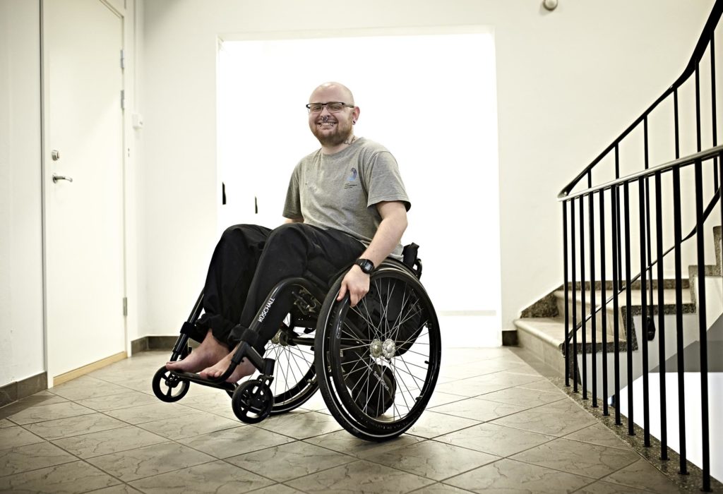 Axel balanserer på bakhjulene på rullestolen og smiler mot kamera.