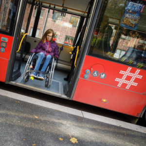 Ingrid Njerve i rullestol i døråpniingen på en rød Ruter-buss i Oslo.