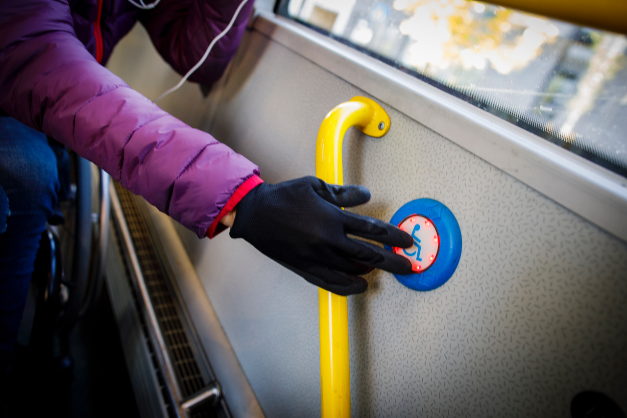 Hånd med finger som trykker på handikap-stopp-knapp inne i buss