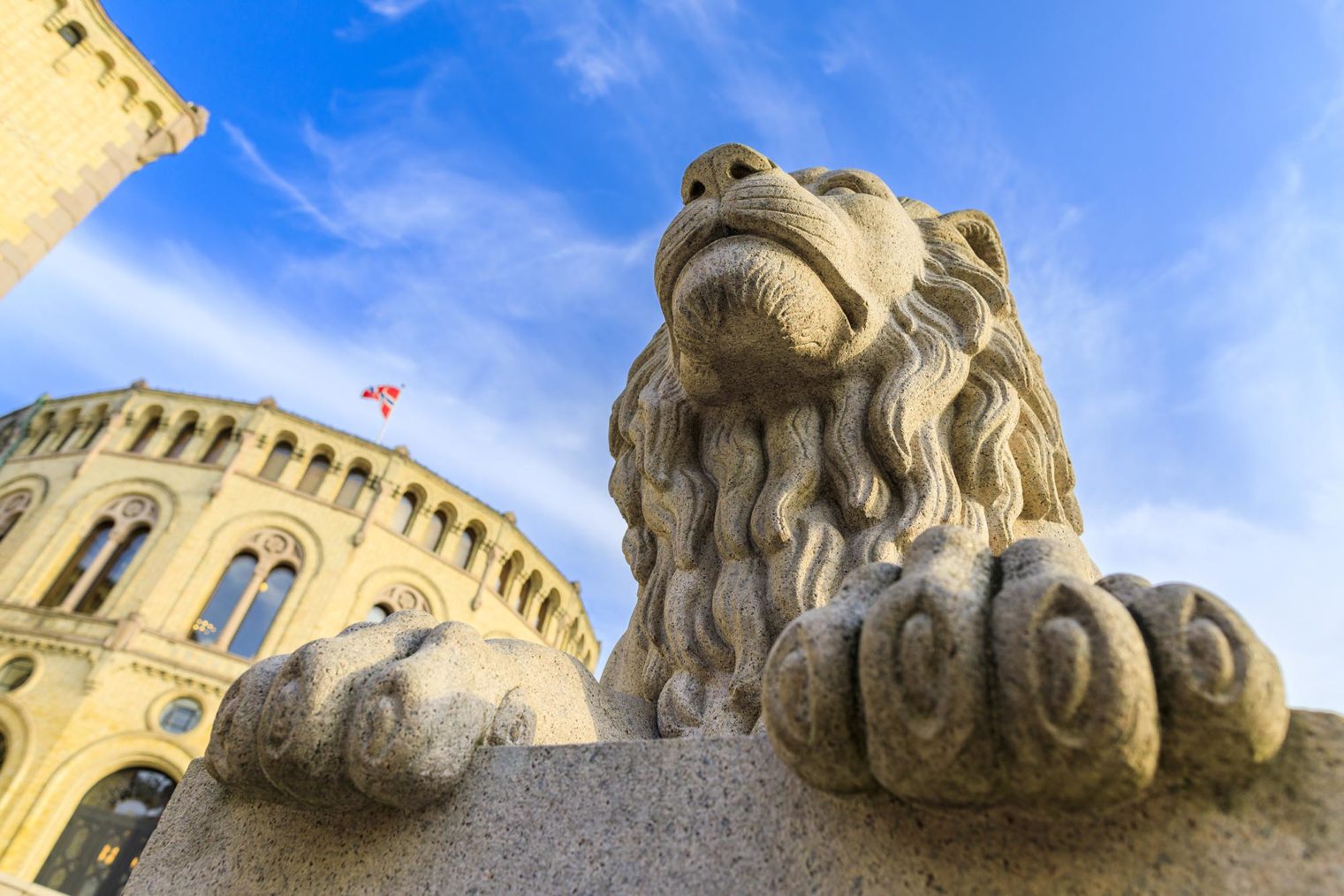 Detaljbilde av en av løvene på Løvebakken med stortingsbygningen i bakgrunnen.