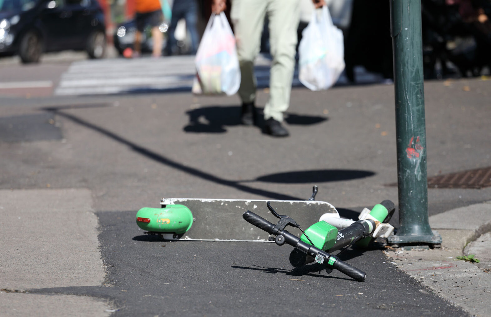 Bilde av mann som kommer gående mot en elsparkesykkel som ligger slengt på fortauet.