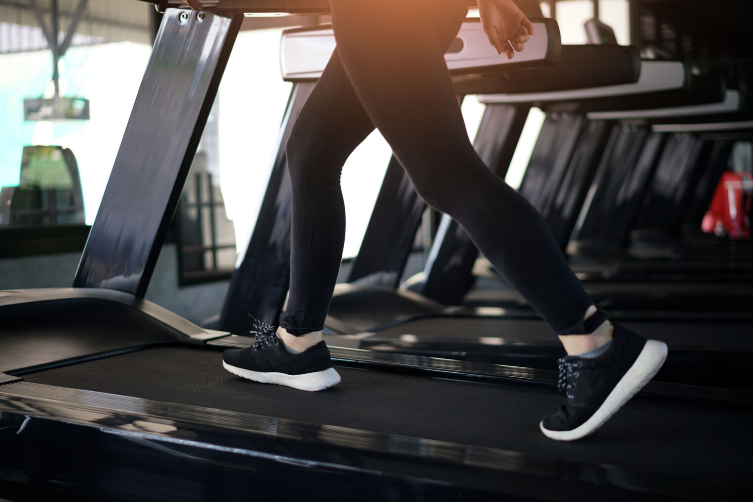 Detaljbilde av bena til en kvinne som løper på en tredemølle på et treningsstudio.