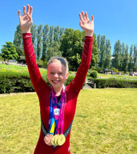 Strekker armene over hodet og jubler. Medaljer rundt halsen.