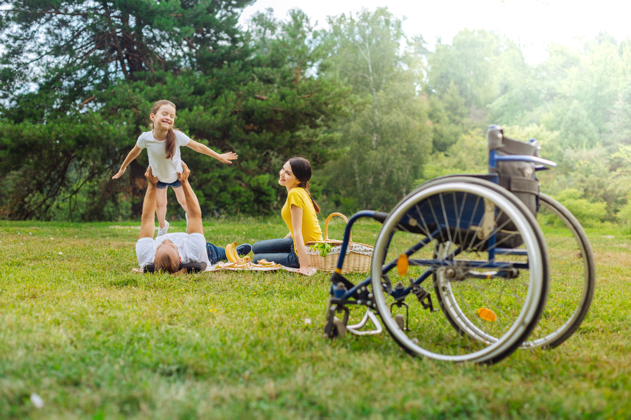 Familie,slapper av i parken. Rullestol i forgrunnen.