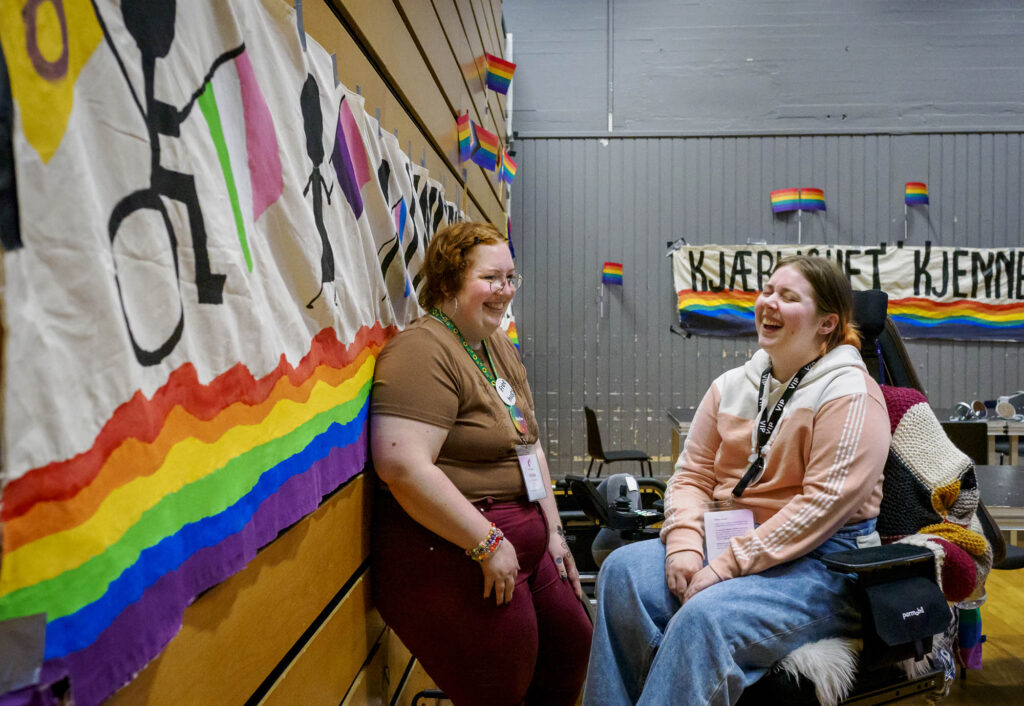 De to snakker sammen og ler i auditoriet der regnbuebannere er hengt på veggene.