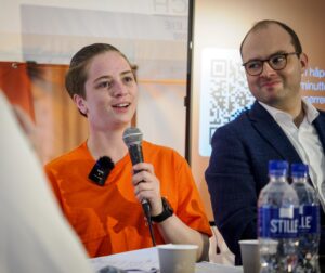 Henriette snakker i mikrofonen, mens statssekretæren ser mot henne og smiler.