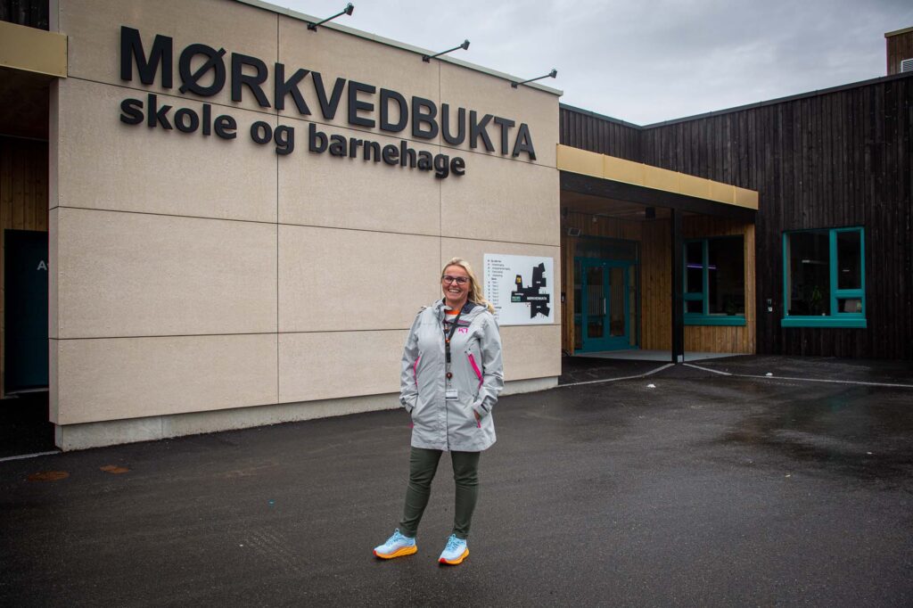 Pettersen poserer utenfor skolen. På veggen bak henne står: Mørkvedbukta skole og barnehage.