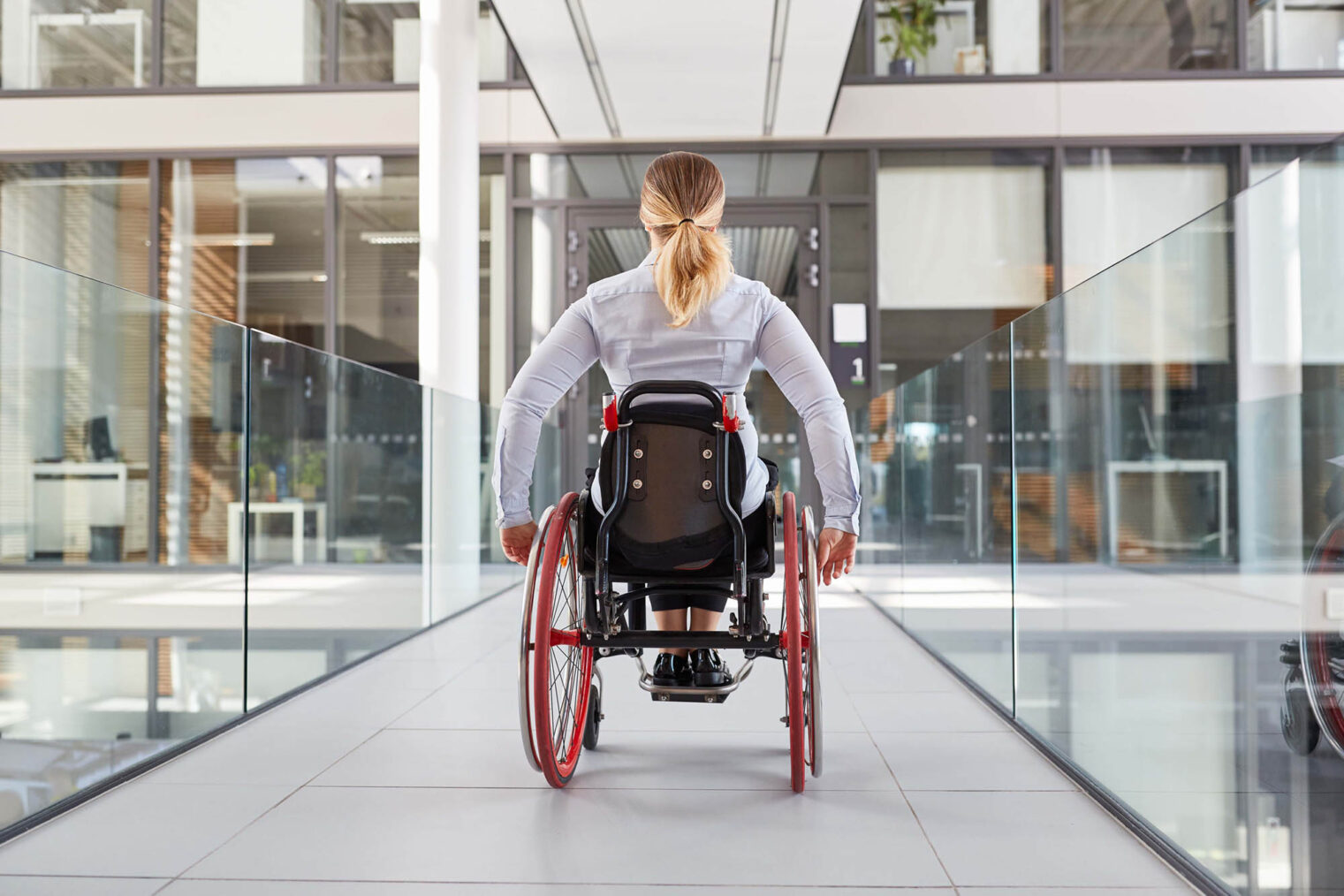 Ung kvinne i rullestol på vei mot inngangsdøren til en kontorbygning.