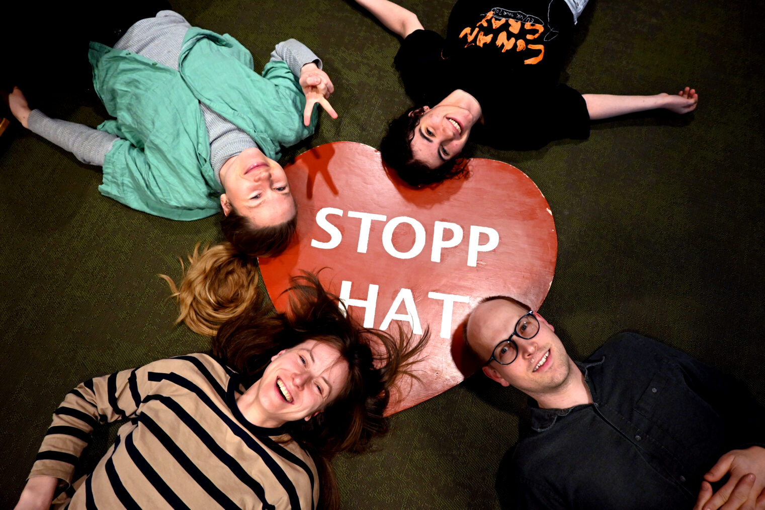 Tre kvinner og en mann ligger på gulvet rundt et papphjerte med teksten "Stopp hat".