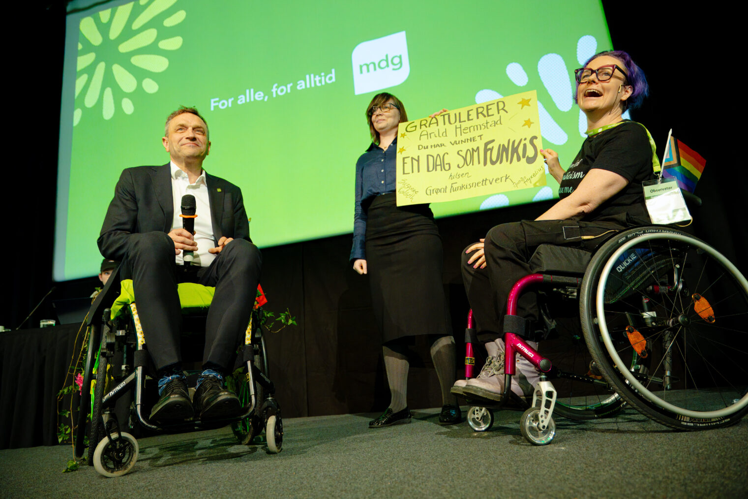 Arild Hermstad i rullestol ved siden av to kvinner med plakaten "Gratulerer! Du har vunnet en dag som funkis"