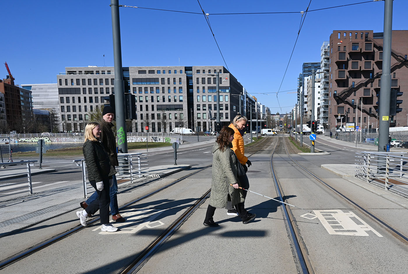 Kvinne med hvit stokk krysser trikkeskinner på fotgjengerfelt sammen med to kvinner og en mann