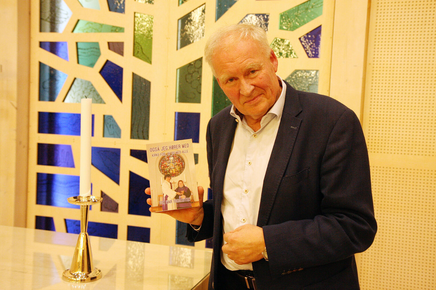 Tor Ivar Torgauten foran glassaltertavle med boka si