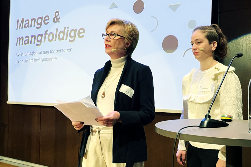 Janne Skei og Henriette Hvarnes Hansen på podiet foran storskjerm med teksten "Mange & mangfoldige"