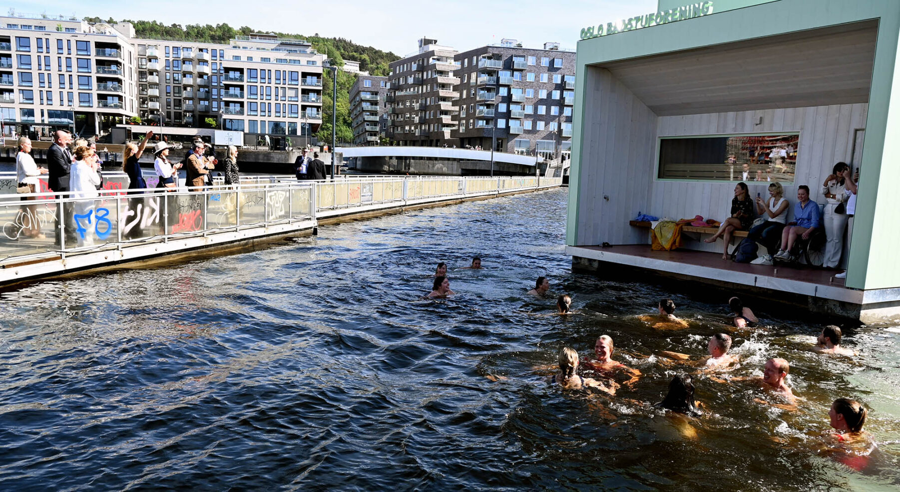 Badstuen Trosten med mange badende i vannet foran