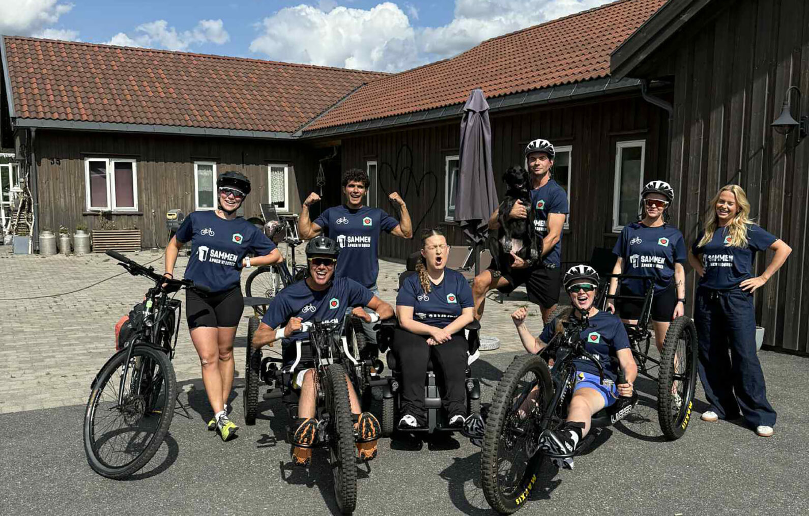 Håndsyklister og en gjeng andre i like T-skjorter foran et hus