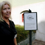 PLAKETT VED INNGANGEN: Folkemuseets arkitekt Cecilie Thue ønsker velkommen inn gjennom den nye inngangsdøra, forbi plaketten som viser at utstillingen er belønnet med pris for god tilgjengelighet.