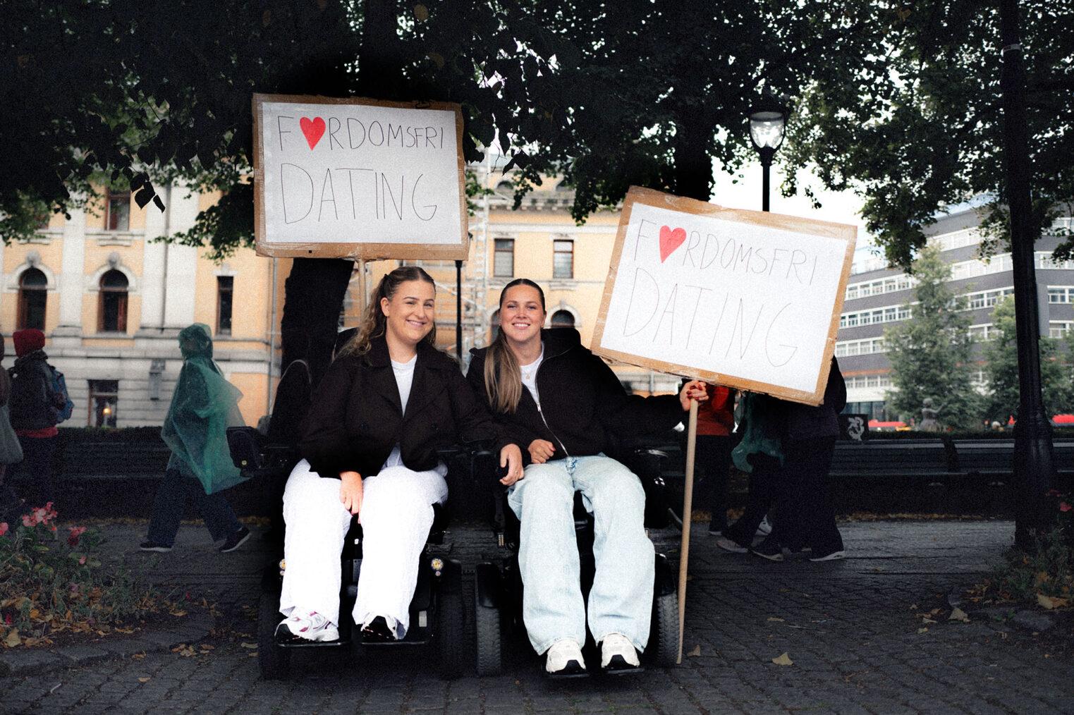 Amalie Rakkestad og Hannah Lunden, begge i elektrisk rullestol, i Studenterlunden med plakater der det står "Fordomsfri dating"