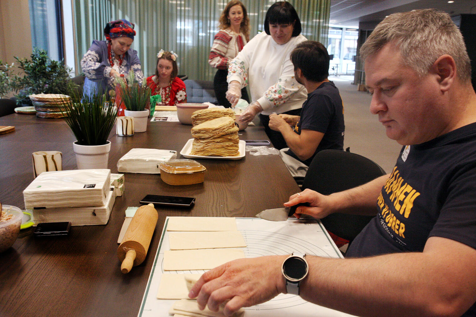Seks mennesker, tre av dem i rullestol, inntil møtebord med kjevle, bakematte og pannekaker