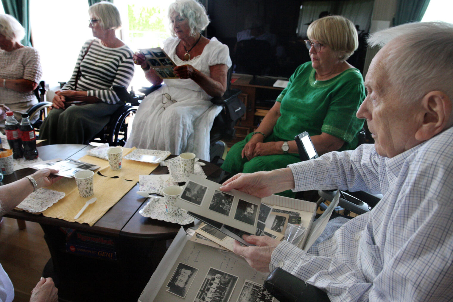John Røvik sitter ved dekket salongbord sammen med flere jevnaldrende kvinner og ser på bilder