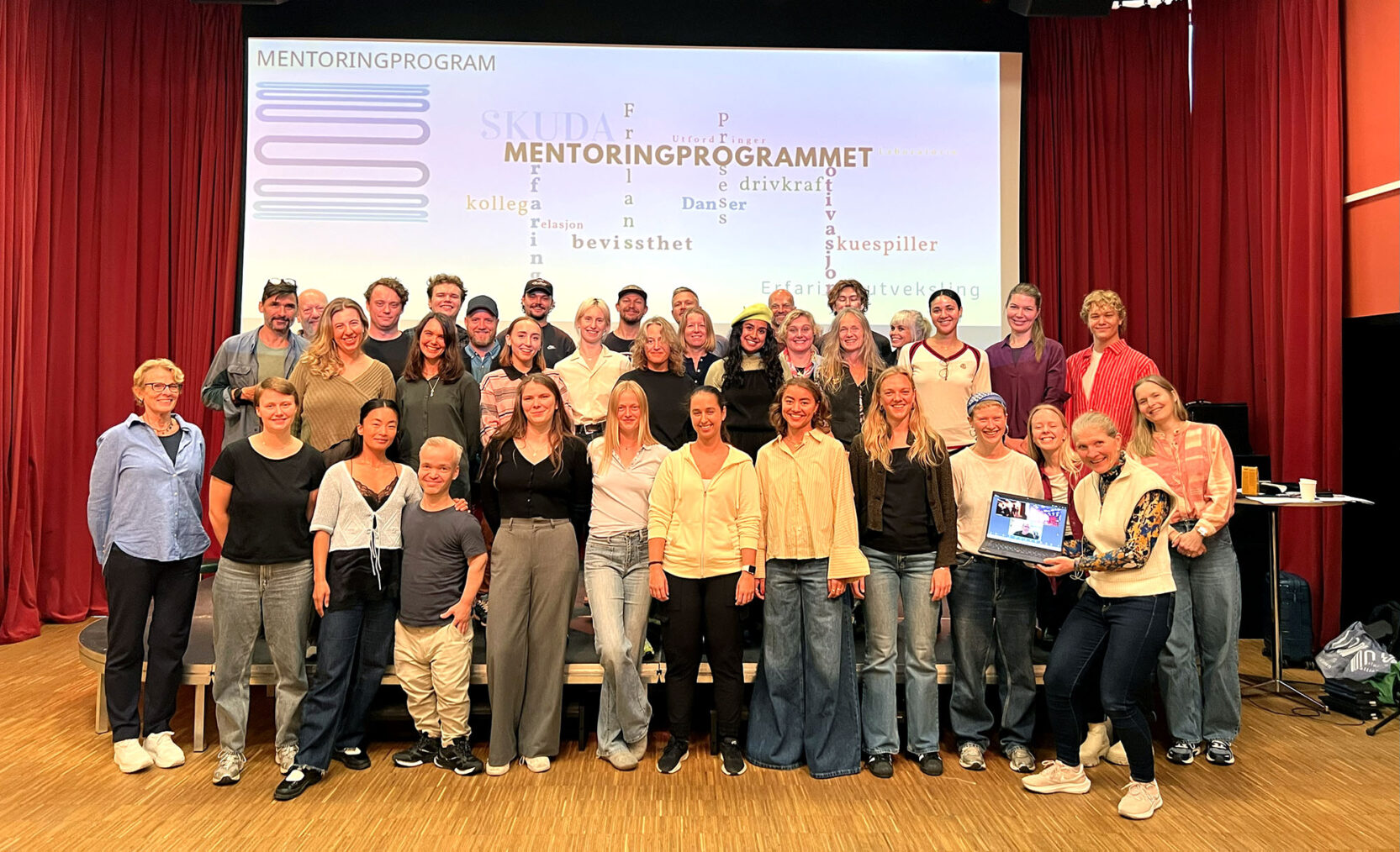 Gruppebilde med et 40-tall mennesker foran en storskjerm hvor det står "Mentoringprogrammet"