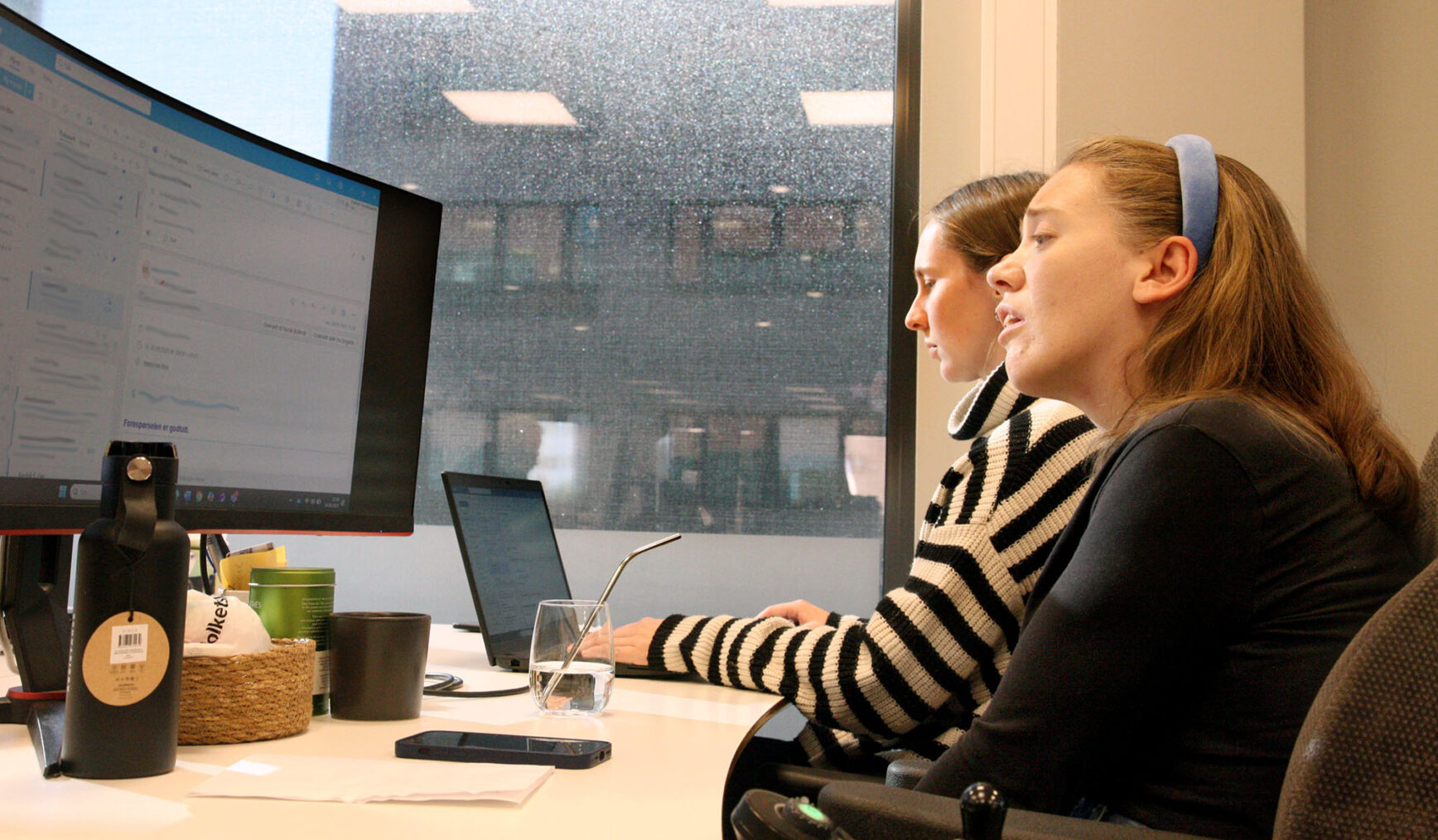 Ida Hauge Dignes ser på stor PC-skjerm mens assistenten skriver på tastaturet i et kontorlandskap