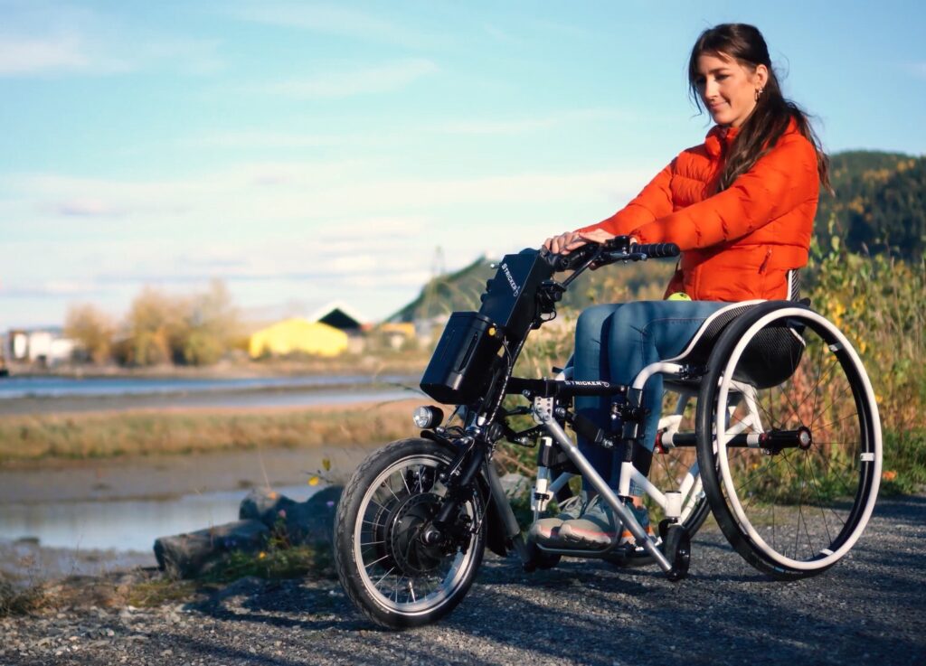 Kvinne kjører rullestol med sykkelfront på grusvei