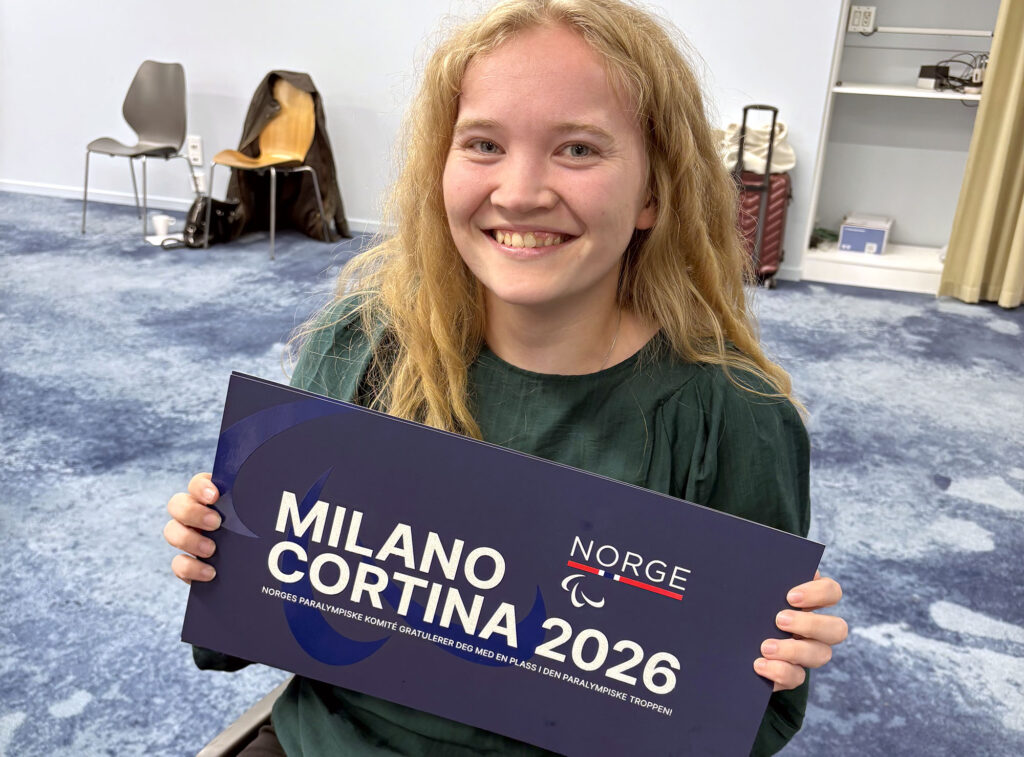 Smilende Mia Larsen Sveberg holder skilt med teksten "Milano Cortina 2026"