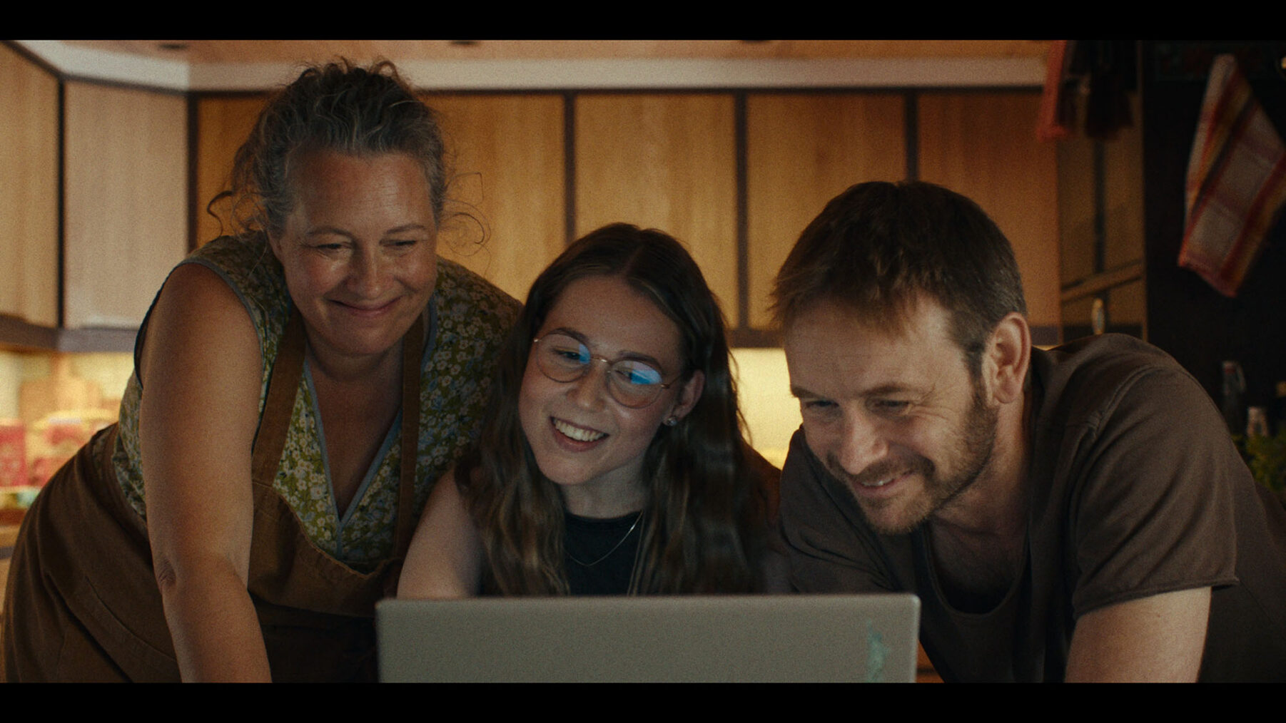 Stillbilde fra Min første kjærlighet der Ella ser på en PC-skjerm sammen med foreldrene sine og smiler