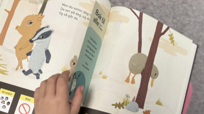Barnehånd blar i barnebok med symboltegninger nederst på siden