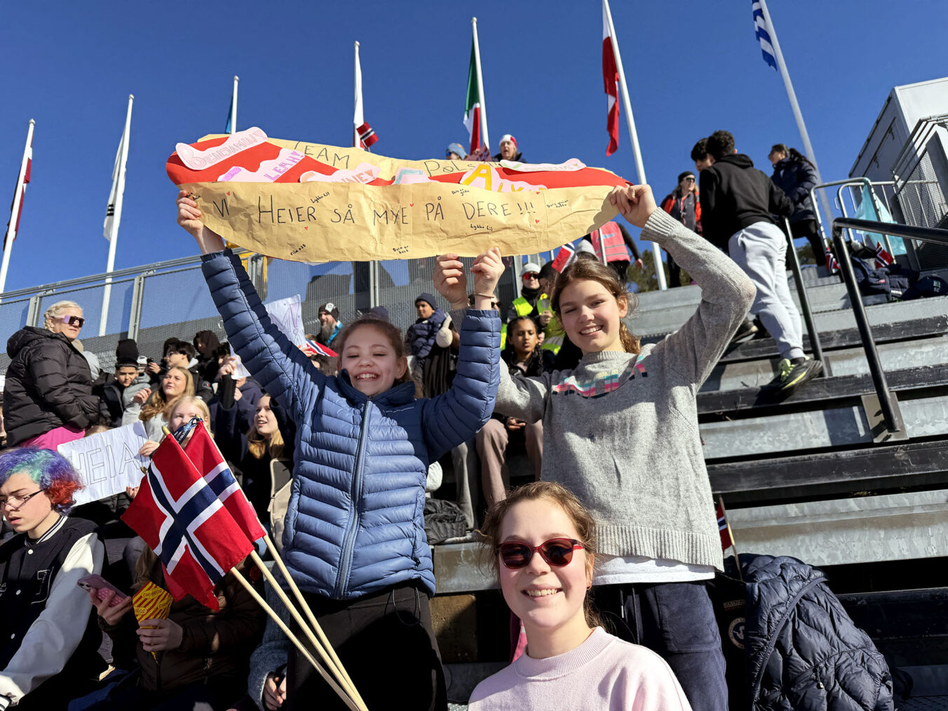 Jenter på tribune i Holmenkollen med flagg og plakat