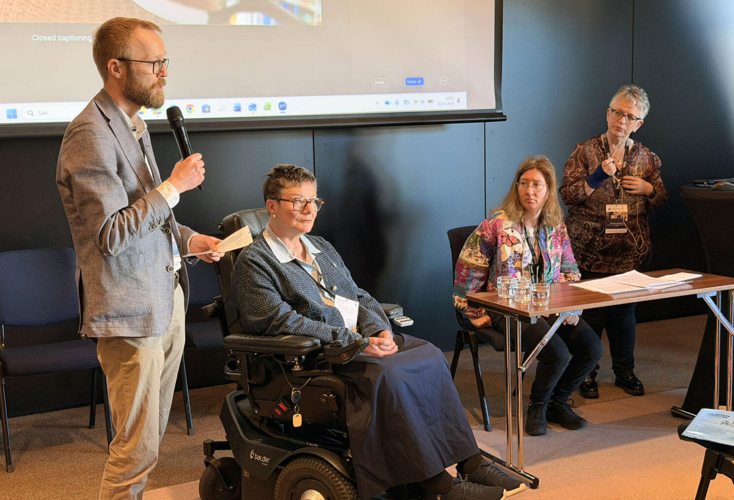 Tove Linnea Brandvik i rullestol mellom Egil Skogseth og Martine Eliasson foran storskjerm. Tolk står ved siden av.