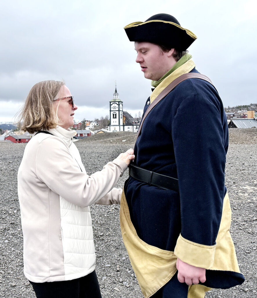 Tone Bratseth retter på uniformsjakka til Christoffer Bratseth, stående på Slagghaugen med Røros kirke i bakgrunnen