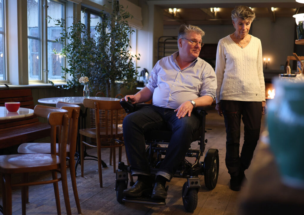 Mann i elektrisk rullestol ved siden av gående kvinne i kafe