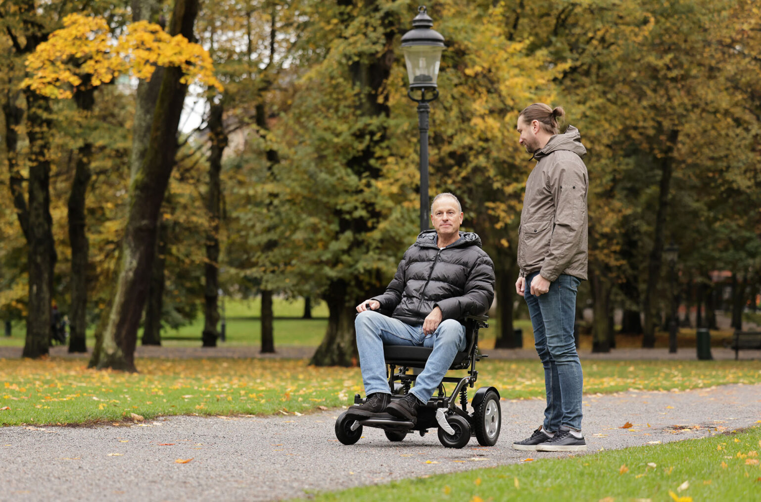 Mann på el-rullestol i park sammen med gående mann