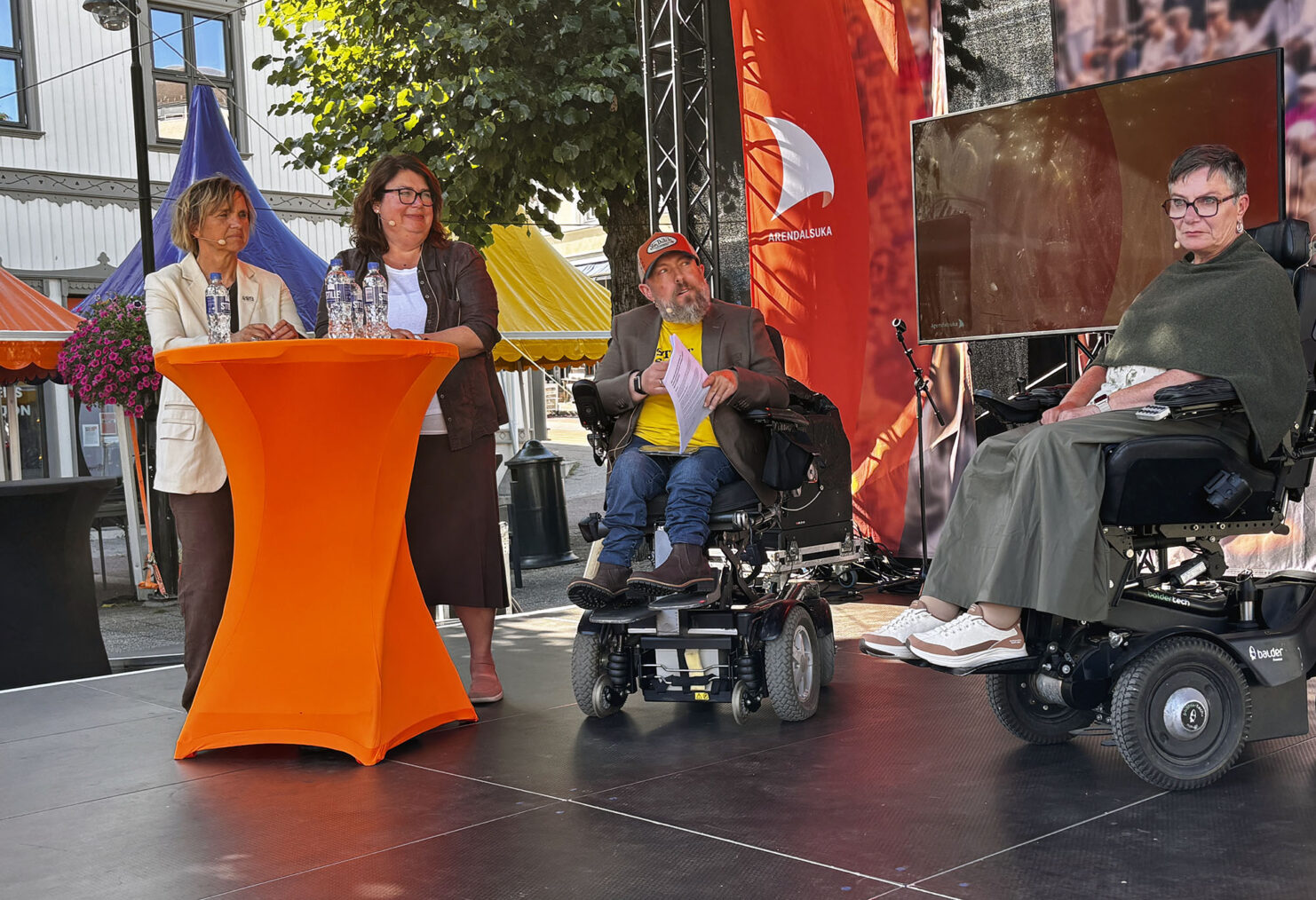 Debattpanel med to stående kvinner, en mannlig og en kvinnelig rullestolbruker på utescene
