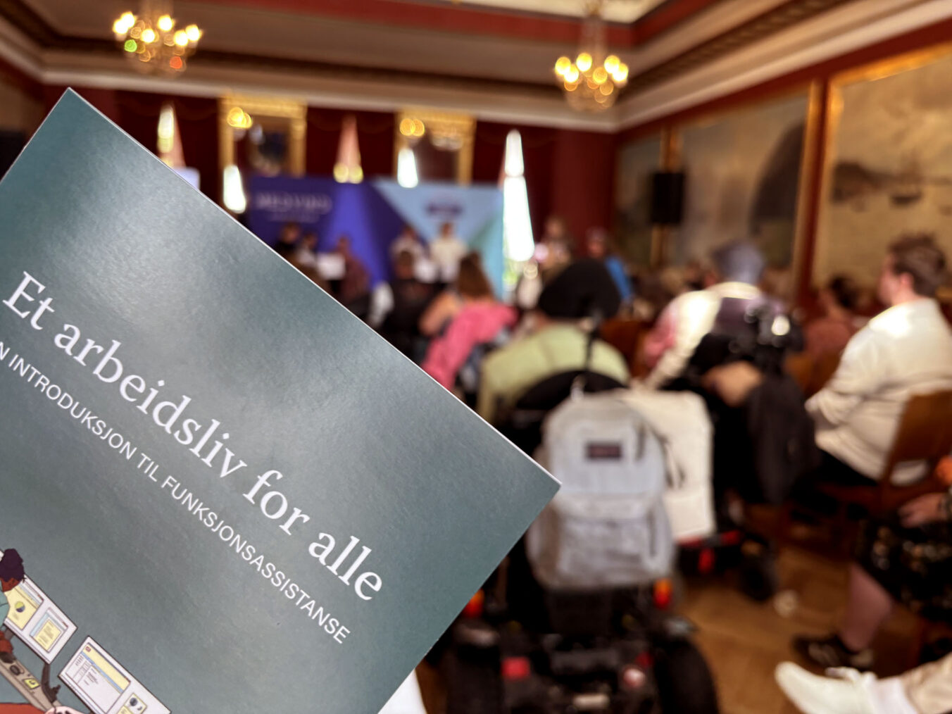 Brosjyre med forsideteksten "Et arbeidsliv for alle", fullsatt møtesal i bakgrunnen.