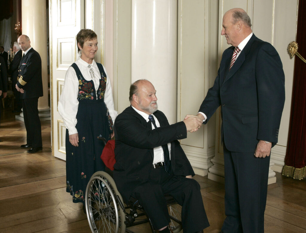 Sverre Bergenholdt i rullestol håndhilser på kong Harald på slottet. Eva-Lisbeth Bergenholdt går bak.
