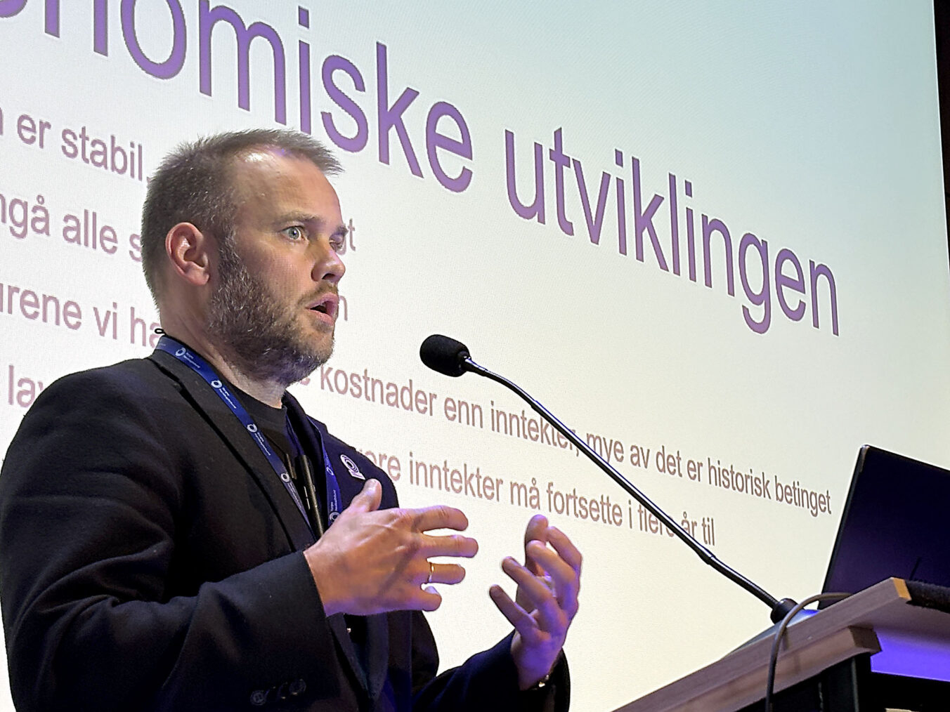 Bjarne Kristoffersen på talerstol foran storskjerm med teksten "Den økonomiske utviklingen"