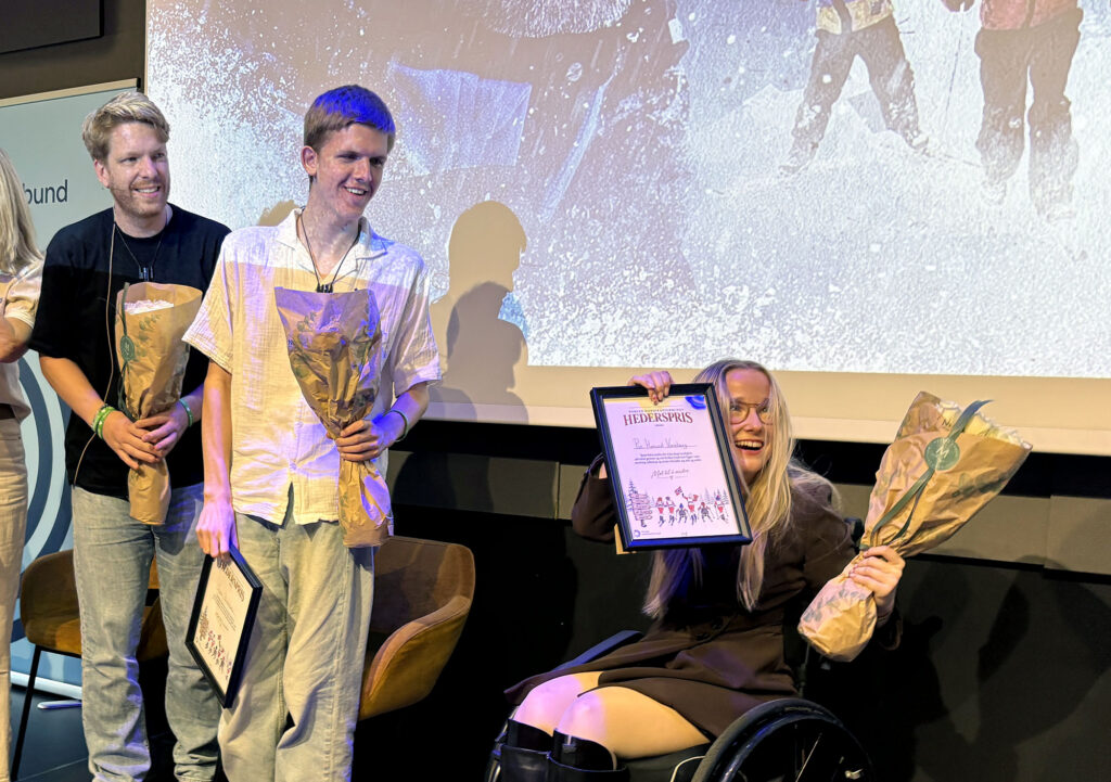 Øyvind og Syver Blindheim og Pia Hasund Vareberg med blomsterbuketter og innrammede diplomer på scenen