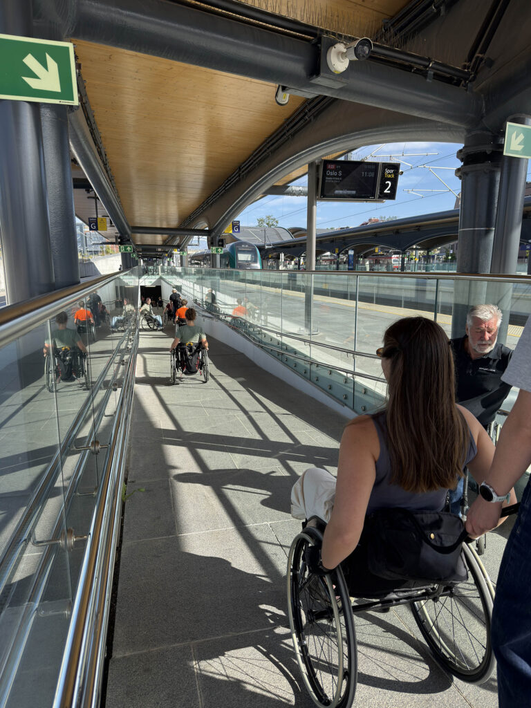 Personer i rullestol på lang rampe på jernbanestasjon